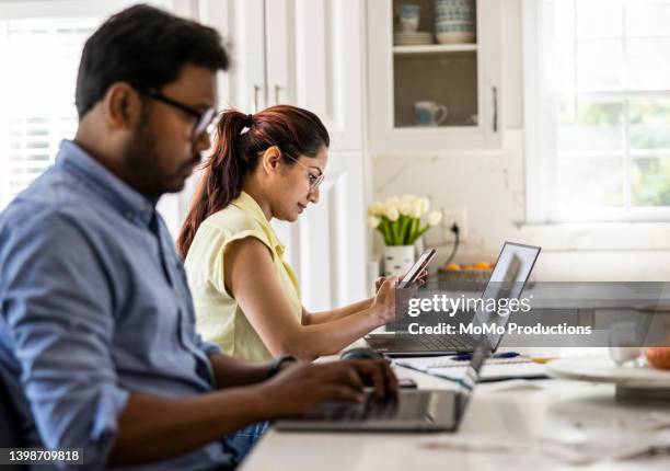 husband and wife using laptop computers in kitchen - indian wife stock pictures, royalty-free photos & images