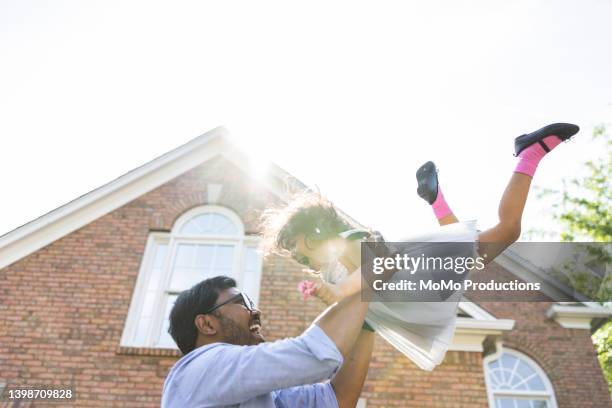 father lifting toddler daughter in the air in front of suburban home - dad throwing kid in air stockfoto's en -beelden