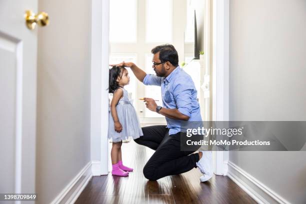 father measuring toddlers daughter's height against wall at home - simple living stock pictures, royalty-free photos & images