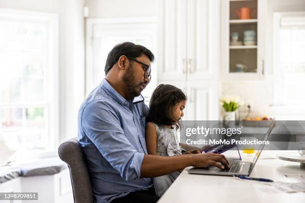 father using laptop and smartphone while holding toddler daughter - man glasses tablet in kitchen stock pictures, royalty-free photos & images