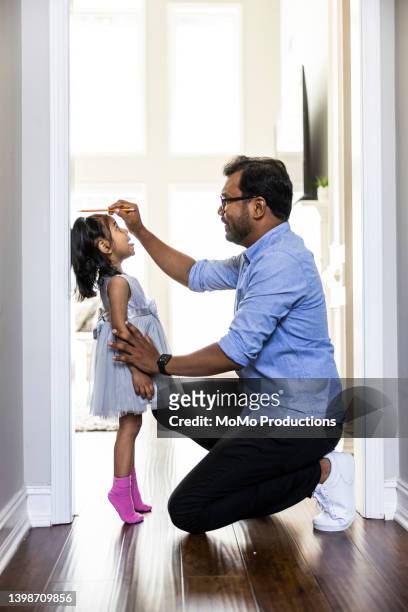 father measuring toddlers daughter's height against wall at home - angelica hale fotografías e imágenes de stock