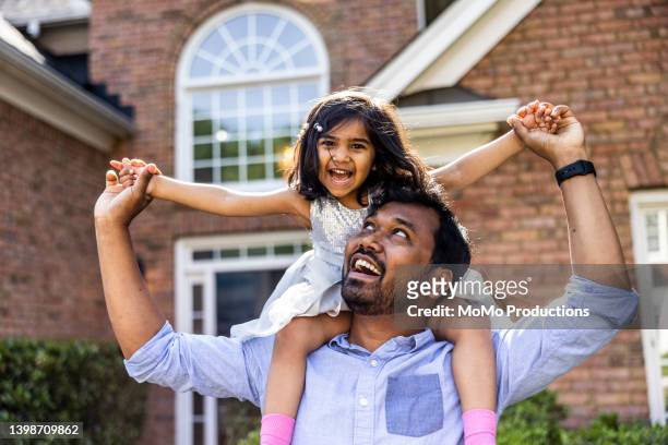 toddler daughter riding on father's shoulders in front of home - indian lifestyle stock-fotos und bilder