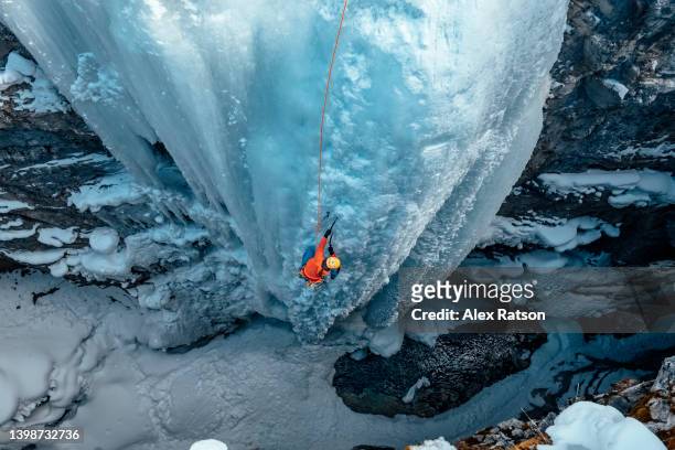 a woman ice climbs up a dramatic frozen waterfall in a deep canyon in the canadian rockies - canadian wilderness foto e immagini stock