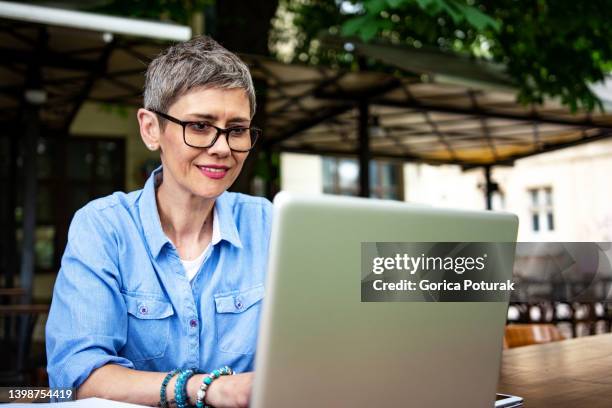 belle femme d’affaires mature aux cheveux courts travaillant sur un ordinateur portable - une seule femme d'âge mûr photos et images de collection