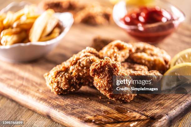 detail of chicken nuggets served on a wooden board with ketchup, baked potatoes and lemon wedges. - chicken fingers stockfoto's en -beelden