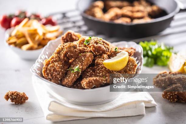 chicken nuggets served in a bowl with lemon wedge and sprinkling of sesame seeds. - chicken fingers stockfoto's en -beelden