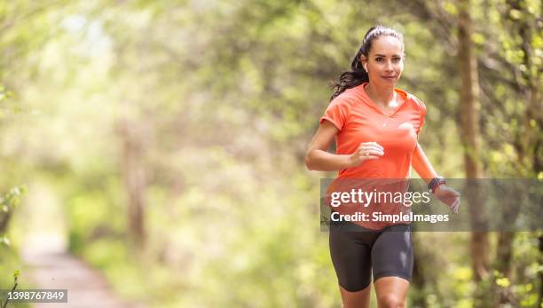 woman running in the woods dressed in bright orange color t-shirt and black shorts. - running shorts foto e immagini stock