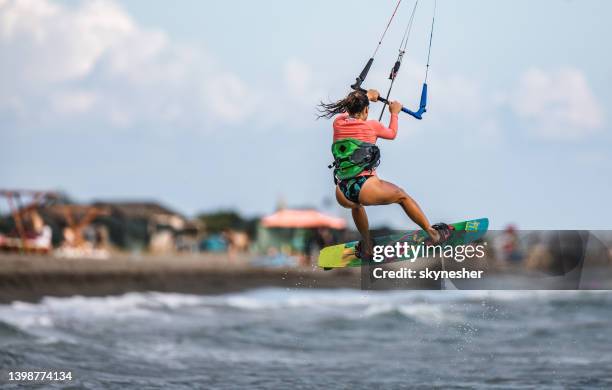 vista posteriore della donna spensierata che salta durante il kiteboard surf in mare. - kite foto e immagini stock
