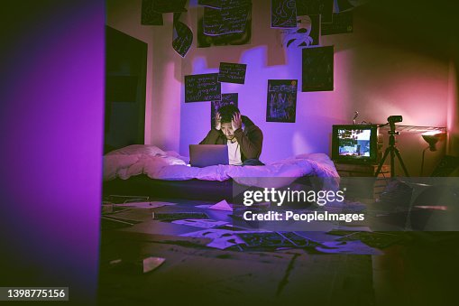Indian man hallucinating and feeling paranoid while using his laptop in his messy bedroom at home. Young man feeling stressed and scared. Schizophrenic thinking he's getting hacked through technology Indian man hallucinating and feeling paranoid while using his laptop in his messy bedroom at home. Young man feeling stressed and scared. Schizophrenic thinking he's getting hacked through technology