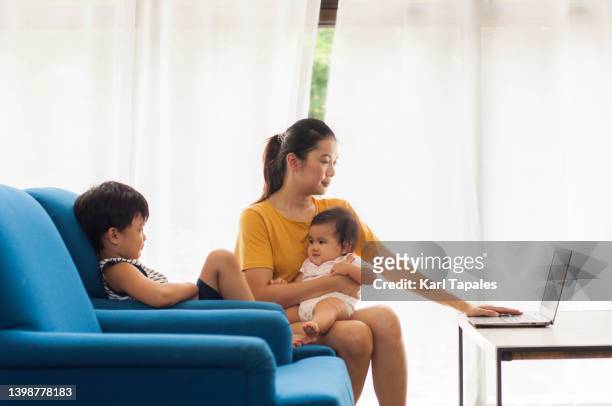 a southeast asian woman is working from home using her laptop with her male and female children - philippines women fotografías e imágenes de stock