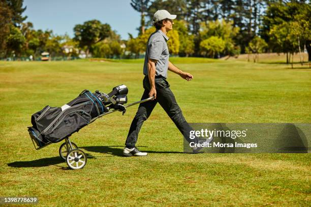male golfer with bag walking on golf course - golftasche ziehen stock-fotos und bilder