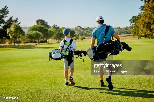 golfer and son with golf bags walking on field - golf sport foto e immagini stock