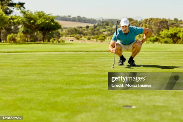 golfer crouching while analyzing field in summer - einlochen golf stock-fotos und bilder