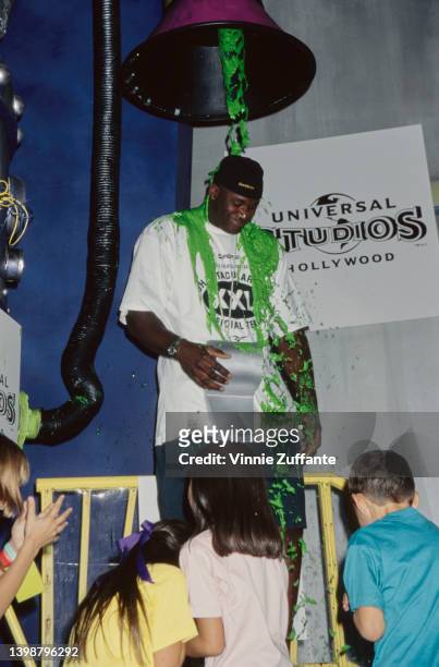Children watch as American basketball player Shaquille O'Neal with a large whistle hanging around his neck is covered with green slime at the 1997...