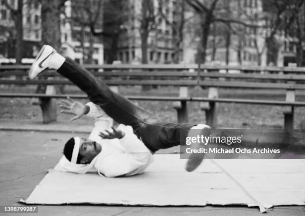 Breakdancer wearing a tracksuit, performs a windmill on a section of cardboard in an park, United States. Circa 1980.