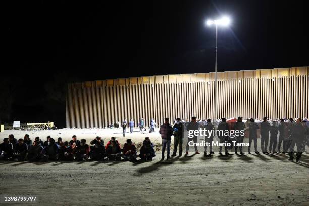 Immigrants wait in the early morning hours to be processed by the U.S. Border Patrol after crossing from Mexico, with the U.S.-Mexico border barrier...