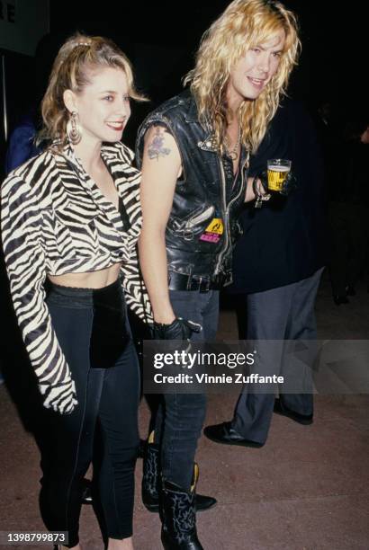 American guitarist and songwriter Duff McKagan, wearing a black leather waistcoat, and his wife, Mandy Brixx, wearing a zebra print crop top, attend...