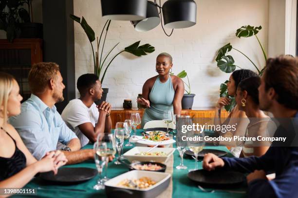 smiling young woman hosting a dinner party for a group of friends - speech dinner stock pictures, royalty-free photos & images