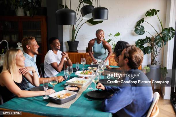 laughing young woman hosting a dinner party for a group of friends - reunião de amigos imagens e fotografias de stock