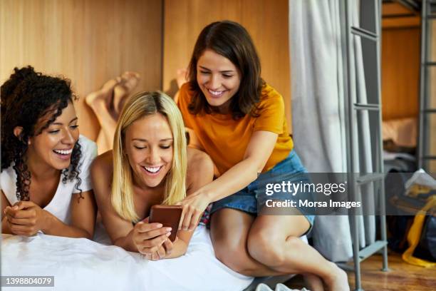 happy female friends sharing cellphone at hostel - bunk beds for 3 stock pictures, royalty-free photos & images