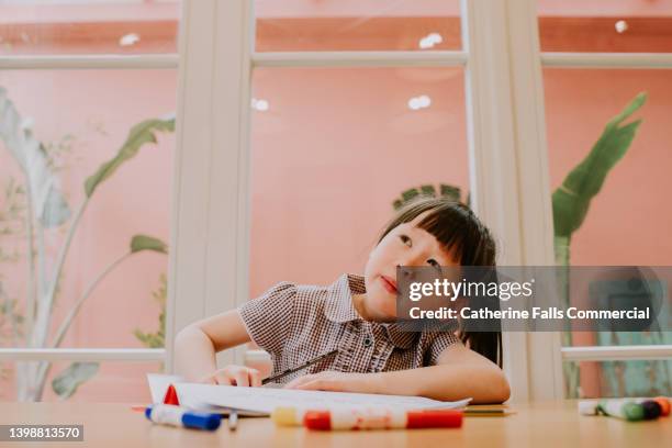 an adorable little girl looks distracted as she stares off into space as she is supposed to be completing a  homework assignment. - adhd stockfoto's en -beelden