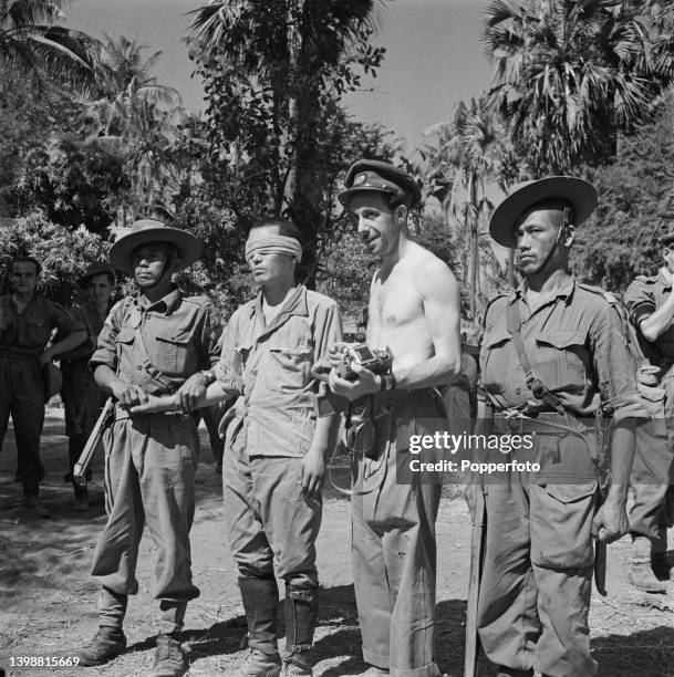 Blindfolded captured Japanese soldier is led by a Gurkha escort through a village near Mandalay in Burma during World War II in March 1945. Allied...