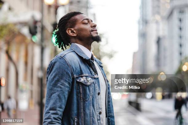 man with his eyes closed stands in the street - black man thinking stock pictures, royalty-free photos & images