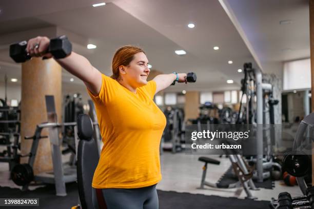 young overweight woman lifting weights in the gym - prop sporting position stock pictures, royalty-free photos & images