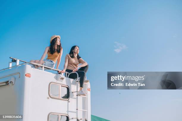 asian chinese lesbian couple enjoying scenic view on top of campervan outdoor road trip during weekend morning - verwonderingsdrang stockfoto's en -beelden