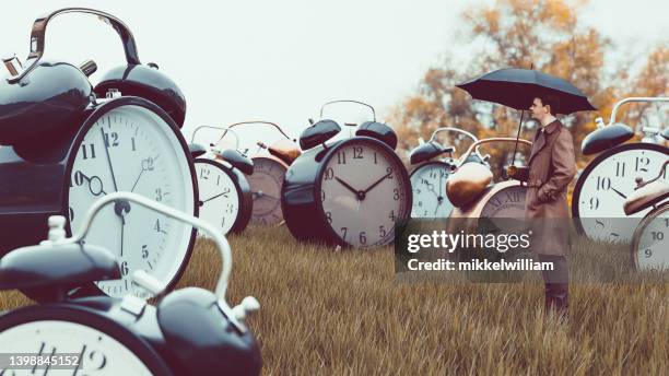 man with umbrella watches big alarm clocks on a field - express stock pictures, royalty-free photos & images