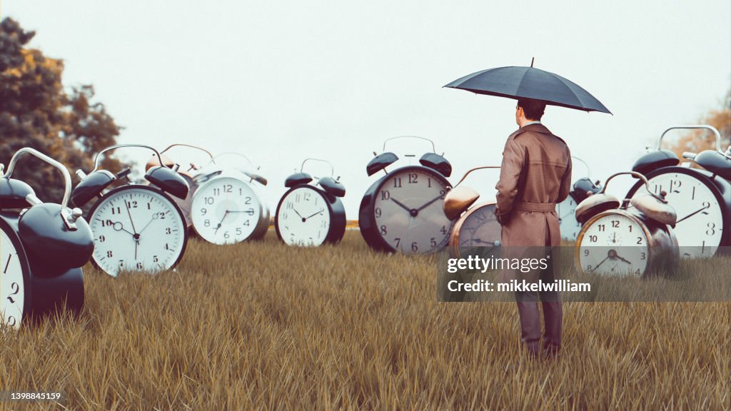 Big alarm clocks on a field in surreal scene with watching