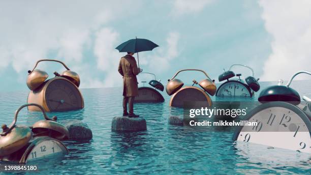 große wecker sind im wasser und mann mit regenschirm beobachtet sie - zeit stock-fotos und bilder