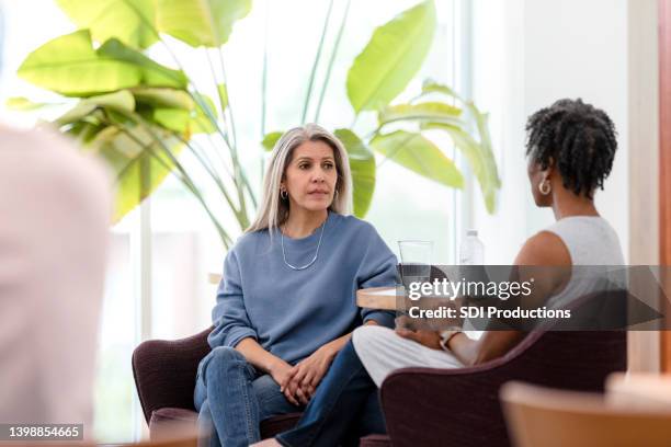 serious mature woman listens to unrecognizable female therapist - mature women cafe stock pictures, royalty-free photos & images