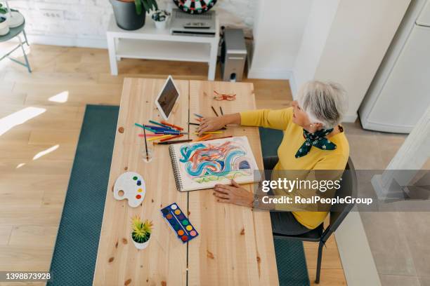 positive senior artist woman paints a picture - illustrator imagens e fotografias de stock