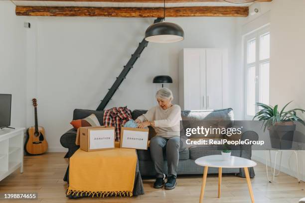 senior woman packing clothes into donation box in living room - possession stock pictures, royalty-free photos & images