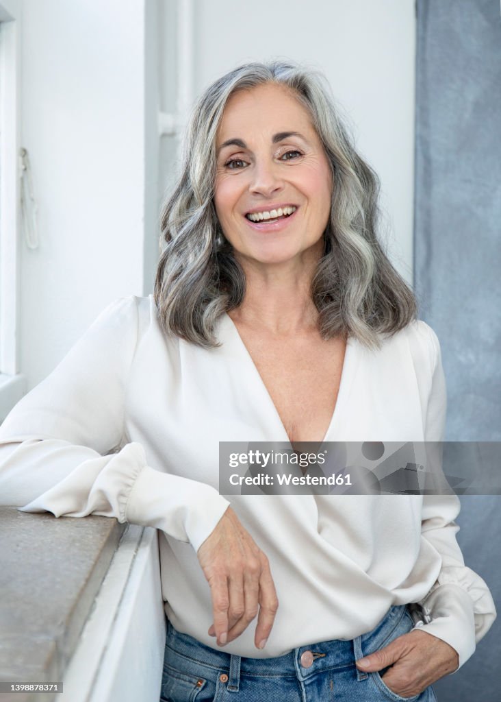 Smiling woman with gray hair standing by window