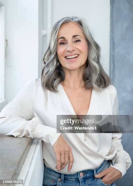 smiling woman with gray hair standing by window - hair woman mature grey hair beauty stock pictures, royalty-free photos & images