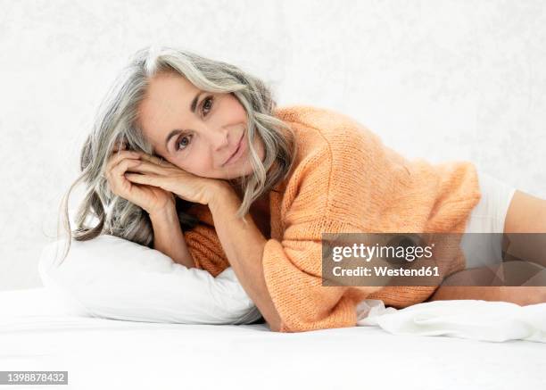 smiling woman lying on bed at home - hair woman mature grey hair beauty stockfoto's en -beelden