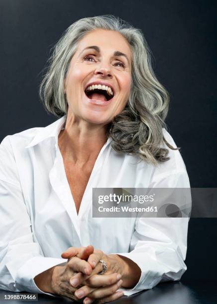 happy woman with hands clasped against black background - beautiful mature woman stock pictures, royalty-free photos & images