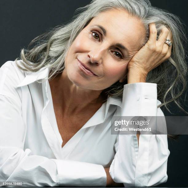 smiling beautiful woman with hand in hair against black background - one grey hair stock pictures, royalty-free photos & images