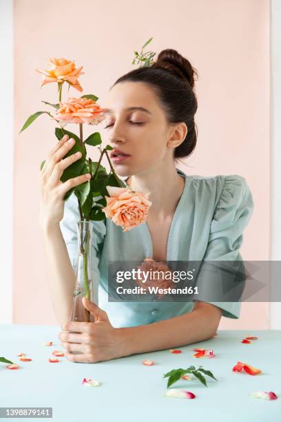 young woman with eyes closed smelling rose against pink backdrop - rose petals stock-fotos und bilder