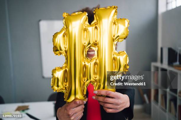 businesswoman holding golden hashtag symbol balloon in front of face - hashtag ストックフォトと画像