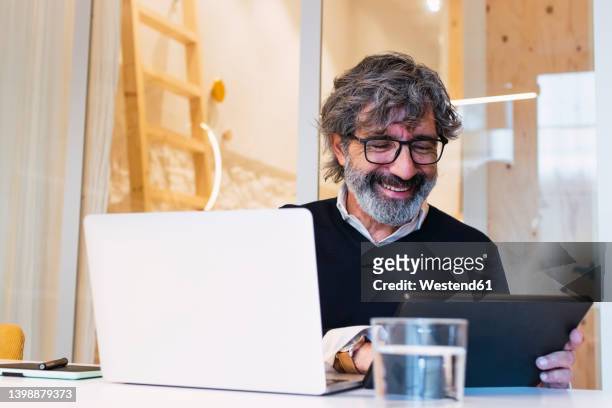 happy senior freelancer using tablet pc sitting with laptop at table - westend61 fotografías e imágenes de stock