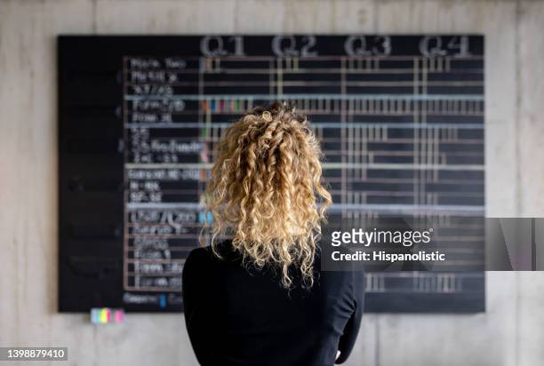mujer de negocios mirando el calendario de gestión de proyectos en su oficina - calendario fotografías e imágenes de stock