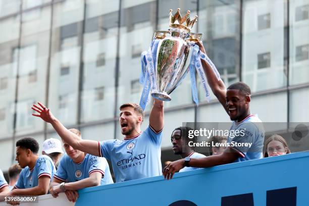 Ruben Dias and Luke Mbete-Tabu of Manchester City lift the Premier League trophy on the parade bus during the Manchester City FC Victory Parade on...