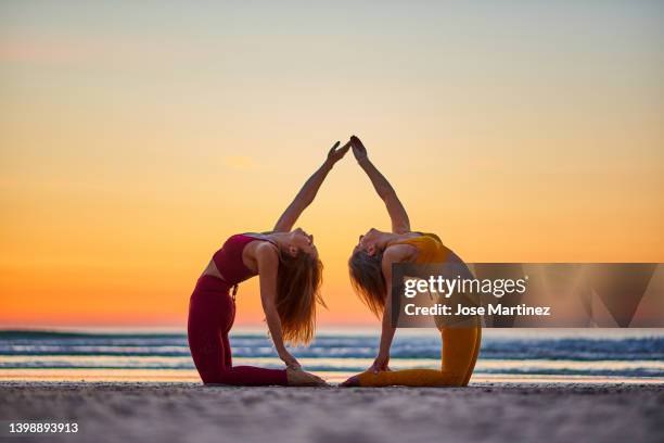 two women doing yoga on the beach at sunrise - acroyoga stock pictures, royalty-free photos & images