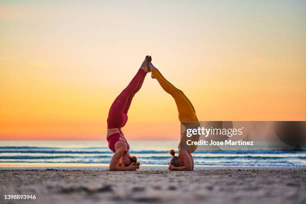 two women doing yoga on the beach at sunrise in the  sirsasana head stand posture - shirshasana stock pictures, royalty-free photos & images