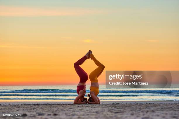 two women doing yoga on the beach at sunrise in the  sirsasana posture - shirshasana stock pictures, royalty-free photos & images