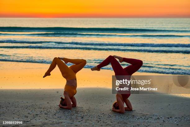 two women doing yoga on the beach at sunrise in the  sirsasana head stand posture - shirshasana stock pictures, royalty-free photos & images