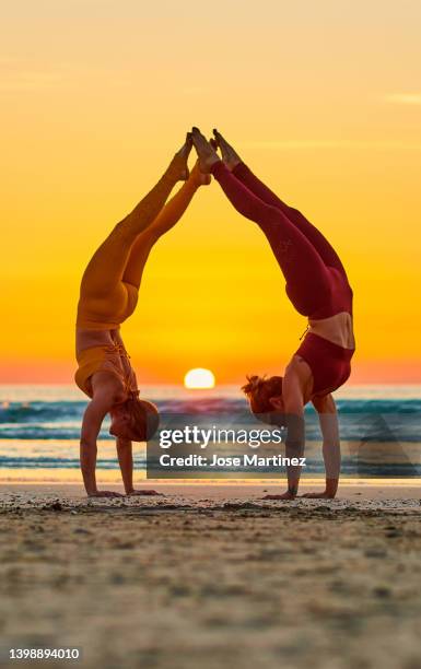 two women doing yoga on the beach at sunrise in the  handstand posture - handstand beach stock pictures, royalty-free photos & images